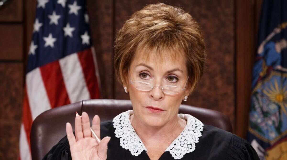 A courtroom-style image of a female judge raising her hand, used in articles discussing Judy McCarthy net worth and public comparisons