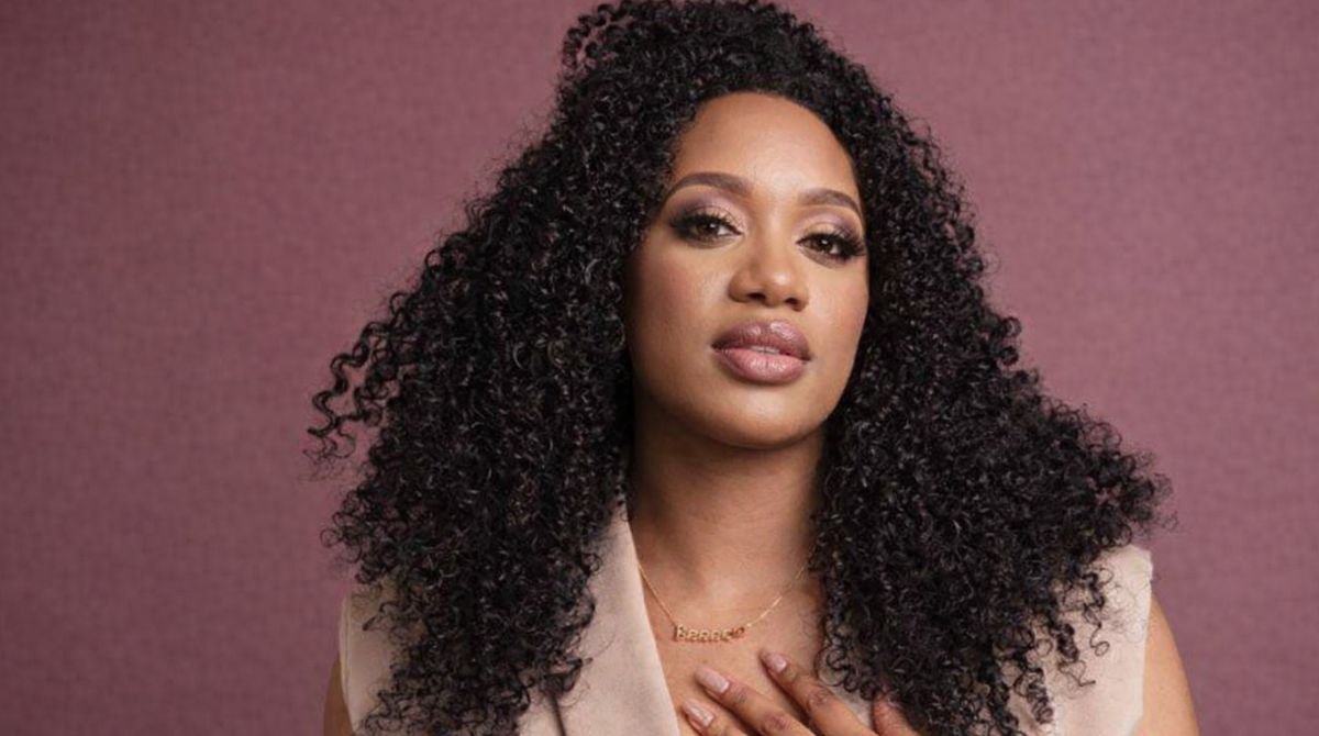 Stormi Steele Net Worth HD portrait with curly hair and mauve background