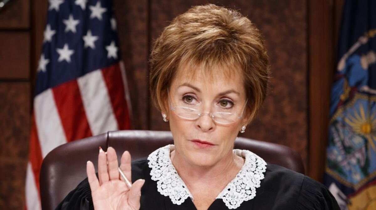 A courtroom-style image of a female judge raising her hand, used in articles discussing Judy McCarthy net worth and public comparisons